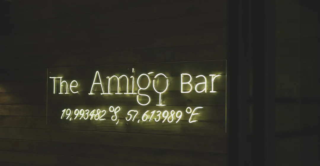 The Amigo Bar & Bistro neon sign showing the venue coordinates